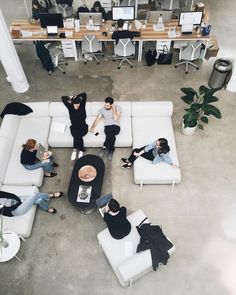 four people sitting on white couches in an open office space with computers and desks