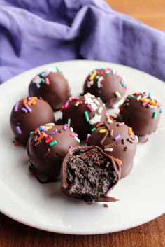 chocolate covered donuts with sprinkles on a white plate next to a purple napkin