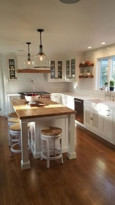 a large kitchen with white cabinets and wooden counter tops, along with stools that match the hardwood flooring