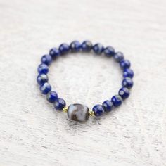 This traditional and bold Dzi bead wrist mala looks amazing on both men and women. Wear it alone for a simple statement or stack it with some of your favorite DharmaShop wrist malas! Powerful lapis beads surround a true agate Dzi bead centerpiece from Taiwan with two gold plated spacers from Thailand. The Dzi bead features a tiger tooth design known to energize the wearer as well as attract good luck and health. Tiger teeth Dzi can assist the owner with concentration, determination, and completi Tiger Teeth, Third Eye Chakra Stones, Tiger Tooth, Tooth Design, Wrist Mala, A Tiger, Third Eye Chakra, Chakra Stones, Third Eye