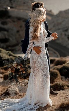 a bride and groom standing on top of a mountain looking at each other with the ocean in the background