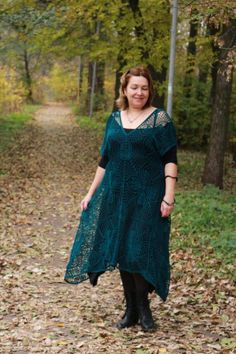 a woman in a green dress standing on a leaf covered path