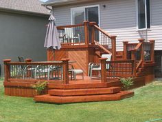 a wooden deck with chairs and an umbrella in the grass next to a house on a sunny day