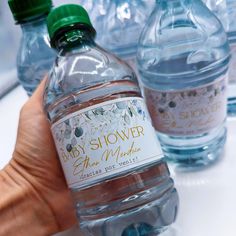 a hand holding a bottle of water in front of several bottled water bottles with labels on them