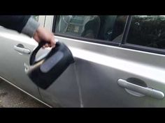 a person is holding a can in front of a silver car with the door open