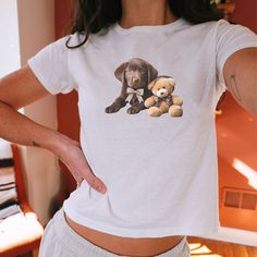 Get ready to LOVE this cute baby tee.  This sweet coquette bowed chocolate lab and teddy bear says Cinnamon Girl!  Grab one for yourself or for a friend. INFORMATION ABOUT THIS PRODUCT AND OUR SHOP POLICIES:  * QUICK FACTS *  This Gildan 5000B crewneck tee is made with midweight fabric that provides a classic and comfortable fit.    Machine wash COLD  Tumble Dry Low  Do not Bleach  Do not Iron  Do not Dry Clean  * SIZING *  👉 We use a "Youth" sized tshirt to achieve the more "authentic" classic baby tee 90's style look. These shirts will fit more like a TRUE mini tee and are not cropped. They will land right about to the waist/hip area and while they will be a bit looser at the waist than at the bust, they are NOT designed to fit skintight like a crop top.  Please see the sizing chart in White Short Sleeve Top With Bear Print, Playful Cotton Tops With Bear Print, Cute Short Sleeve T-shirt With Bear Print, Cute Bear Print Short Sleeve Tops, Cute Bear Print Top With Short Sleeves, Cute Short Sleeve Tops With Bear Print, Cute Short Sleeve Top With Bear Print, White Graphic Tee With Bear Print, Cute Bear Print Crew Neck T-shirt