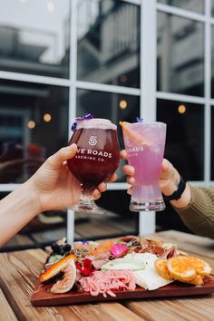 two people holding up wine glasses with food on the table