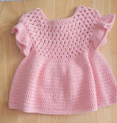 a pink crocheted dress sitting on top of a wooden floor