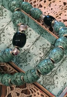 a green and black beaded bracelet with matching beads on a lace doily next to a wooden box