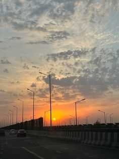 the sun is setting over an empty highway with cars driving down one side and street lights on the other