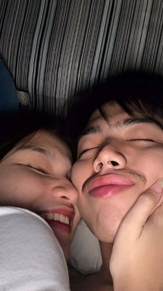 two people laying in bed with their faces close to each other and one person has his eyes closed