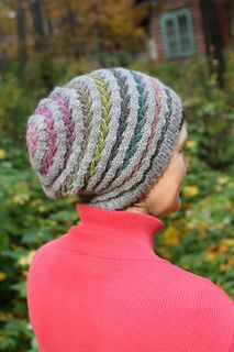 a woman wearing a knitted hat standing in front of some bushes and trees with her back turned to the camera