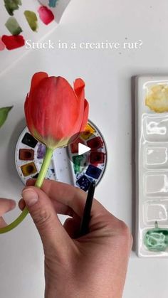 a person is holding a flower and painting it with watercolors on the table