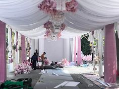 people are standing under a white canopy with pink flowers on the floor and in front of it