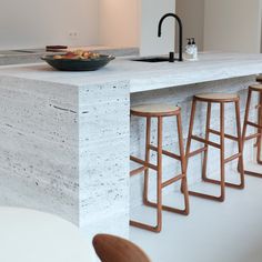 a bowl of fruit sitting on top of a counter next to stools and a sink