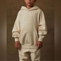 Kids Essential Fear Of God Hoodie New With Tags Attached & Includes Essentials Zip Bag Color- Eggshell (Cream, Light Beige) Size- 6/7 (Kids Unisex) Small Approx. Measurements- Pit To Pit-19 1/2” Length- 20” (Shoulder To Hem) Sleeve Length- 18” (Seam To Cuff) Kids Fear Of God Egg Shell Hoodie The Essentials Fear Of God Kids Egg Shell Hoodie Features An Oversized Fit, Long Sleeves, An Attached Hood, A Bold 1977 Graphic On The Front, And A Rubber Brand Logo On The Hood. Solid Color Hoodie Brushed B Oversized Winter Sweatshirt, Essentials Fear Of God, Egg Shell, Girls Outerwear, Brand Label, Tech Fleece, Fear Of God, Egg Shells, Oversized Fits