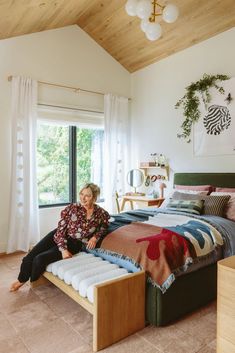 a woman sitting on top of a bed in a bedroom next to a large window