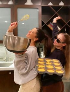 two young women are cooking cookies in the kitchen and one is holding a spatula