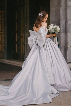 a woman in a white wedding dress is standing on the sidewalk with her back to the camera