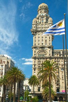 a tall building with a flag flying in the air next to palm trees and buildings