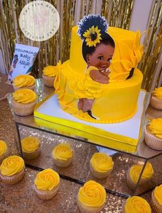 a yellow cake and cupcakes on a table with gold sequins around it