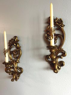 two gold wall sconces with candles on them against a white wall in a room