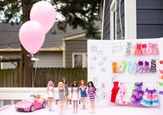 there are many barbie dolls standing in front of a wall with clothes and balloons on it