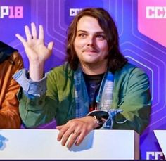 two men sitting at a table with their hands in the air and one holding up his hand