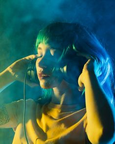 a woman with blue hair is holding a microphone and listening to music on her headphones