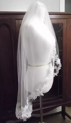 a white wedding veil on top of a mannequin's head in front of a wooden cabinet