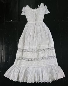 A beautifully decorative little Christening gown dating to the 19th century. Light weight cotton, the bodice is vertically pleated front and back, fastening with ties. At the front are bands of crochet lace on each side, with flounces of floral embroidered whitework running up and around the neck. Under the flounce are short sleeves, embroidered tulle lace with a scalloped edge. The skirt is pleated in to the waist, opening out to a narrow bell shape with alternating bands of pleats, lace and em Victorian Cotton Dress With Historical Design, Cotton Victorian Dress For Daywear, Vintage Cotton Victorian Wedding Dress, White Victorian Cotton Dress, Victorian Cotton Prairie Dress For Daywear, White Historical Dress For Daywear, Victorian Cotton Dress With Broderie Anglaise, White Cotton Victorian Dress, White Cotton Regency Style Prairie Dress