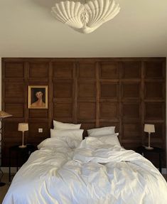 a bed with white sheets and pillows in front of a wooden headboard that has a painting on the wall