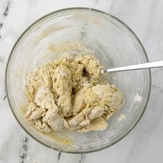 a glass bowl filled with dough on top of a marble countertop next to a metal spoon