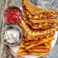 a person holding a plate with french fries and ketchup on it next to other foods