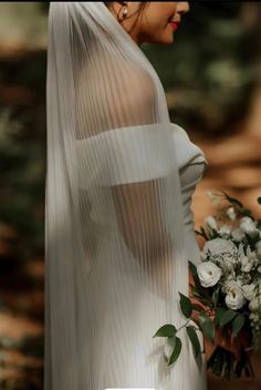 a woman in a white dress holding a bouquet and wearing a veil with flowers on it