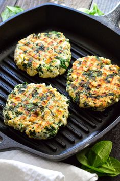 three patties are cooking on a grill with spinach leaves next to the pan