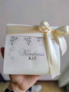 a person holding up a wedding kit with a bow on it's head and ribbon around the package