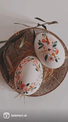 two decorated eggs sitting on top of a plate with leaves and flowers painted on them