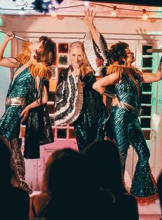 three women are dancing on stage with their hands in the air