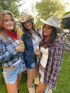 three beautiful young women standing next to each other wearing cowboy hats and holding drinks in their hands