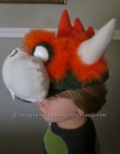 a young boy wearing an orange and black monster hat with horns on it's head