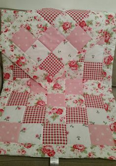 a pink and white patchwork quilt with roses on the front, sitting on a couch