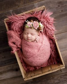 a newborn baby is wrapped in a pink blanket and wearing a flower headband while laying on a wooden crate