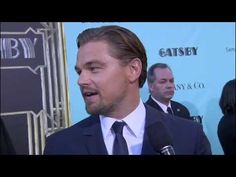 a man in a suit and tie talking to someone on the red carpet at an event