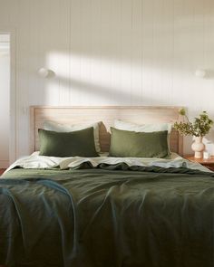 a bed with green sheets and pillows in a white room next to a wooden floor