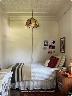 a bedroom with a bed, desk and chair in it next to a lamp hanging from the ceiling