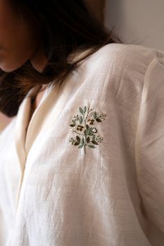 a close up of a person wearing a white shirt with embroidered flowers on the chest