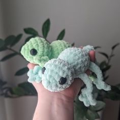 two small crocheted animals sitting on top of each other in front of a plant