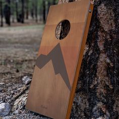 a wooden board with mountains on it next to a tree in the woods and rocks