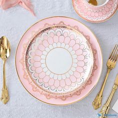 a pink and gold plate with flowers on it next to two forks, spoons and a cup